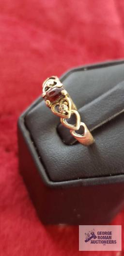 Gold colored ring with heart cutouts, red gemstone, and two clear gemstone chips, marked 10K,