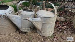 Three vintage watering cans with hand tools
